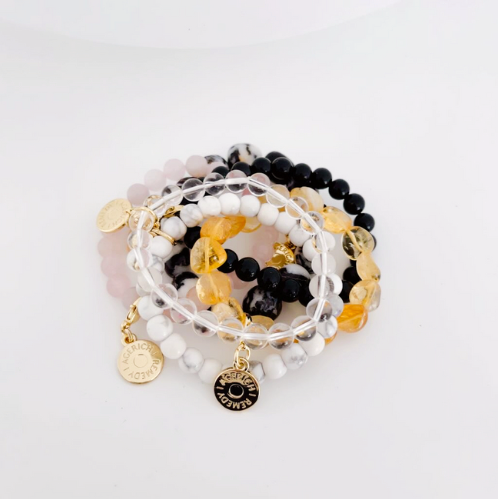 Group of crystal bracelets stacked on top of each other. Featuring a white howlite, clear quartz, rose quartz, black obsidian, zebra jasper and citrine crystal bracelet